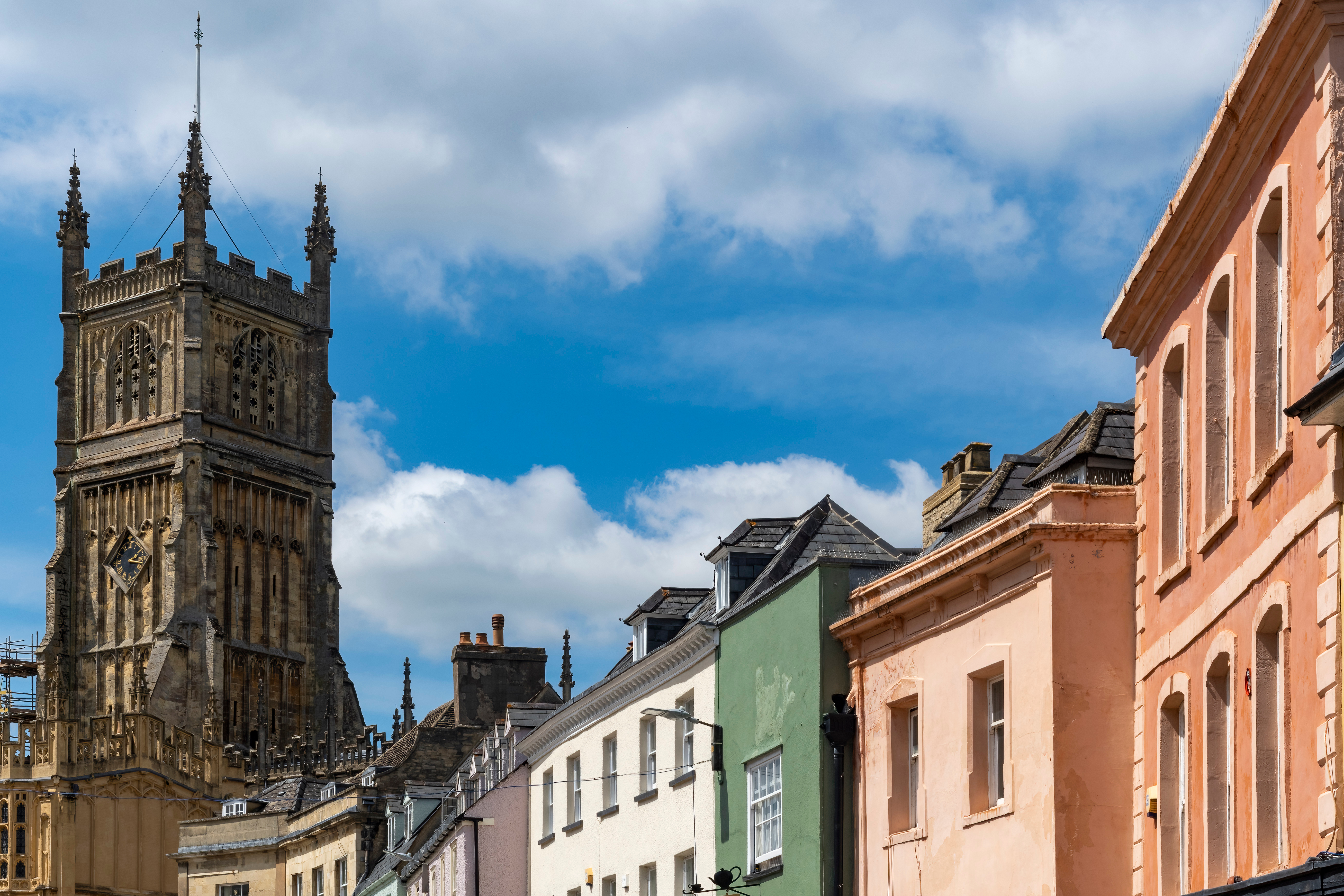 Historisk kirketårn i Cirencester med farverige georgiske bygninger i Cotswolds, England