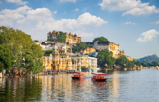 Det historiske City Palace og turistbåd på Lake Pichola i Udaipur, Rajasthan, med smukke refleksioner i vandet ved solnedgang