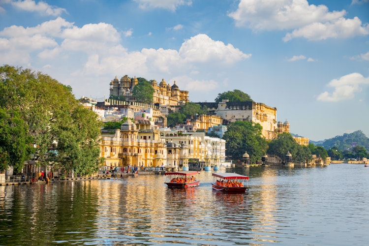 Det historiske City Palace og turistbåd på Lake Pichola i Udaipur, Rajasthan, med smukke refleksioner i vandet ved solnedgang