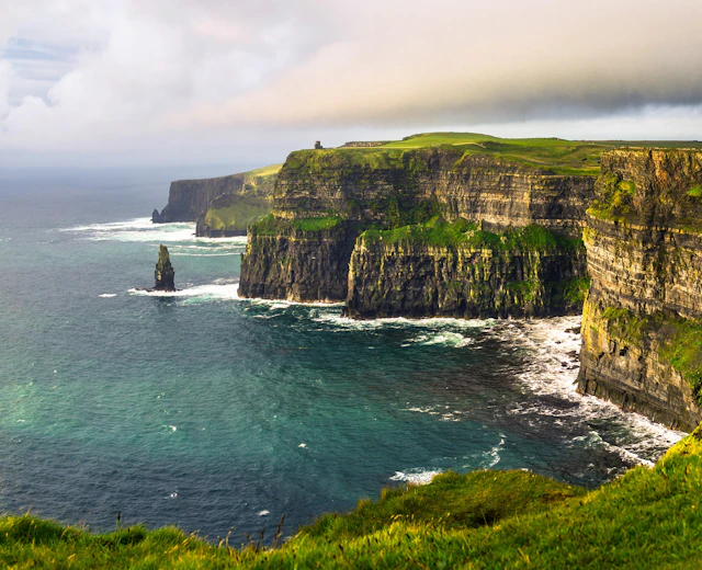 Cliffs of Moher Irland - dramatiske grønne klipper ved Atlanterhavet med bølger og blå himmel