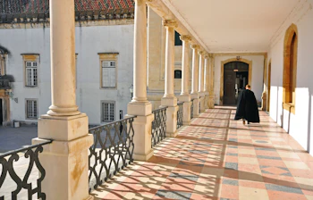 Studerende vandrer gennem den majestætiske søjlegang ved hovedbygningen af Coimbra Universitet i Portugal, en UNESCO verdensarv med klassisk arkitektur og historisk betydning