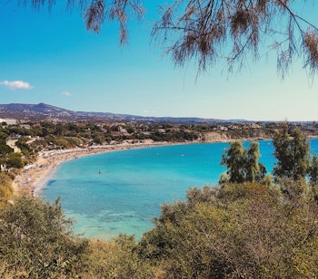 Idyllisk udsigt over Coral Bay stranden i Paphos, Cypern med krystalklart blåt vand, sandstrand og luksuriøse ferieresorts