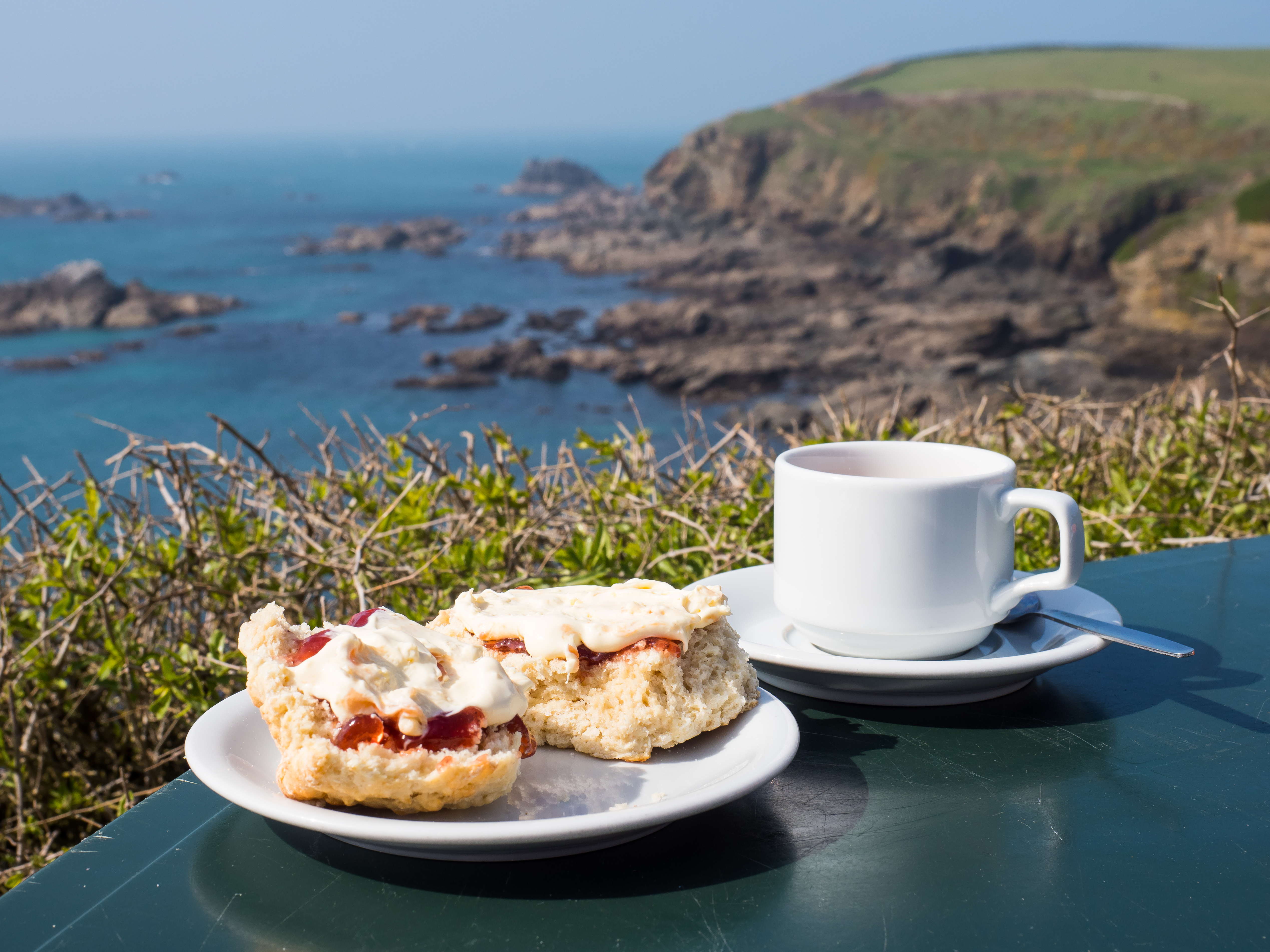 Traditionel engelsk cream tea med scones og clotted cream nydt med udsigt over den dramatiske kystlinje ved Lizard Point i Cornwall