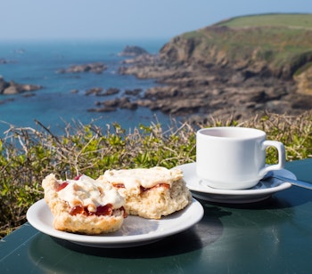 Traditionel engelsk cream tea med scones og clotted cream nydt med udsigt over den dramatiske kystlinje ved Lizard Point i Cornwall