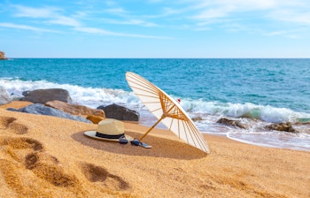 Idyllisk strandscene fra Costa Brava i Spanien med solhat og parasol på den gyldne sandstrand - perfekt til en afslappende sommerferie