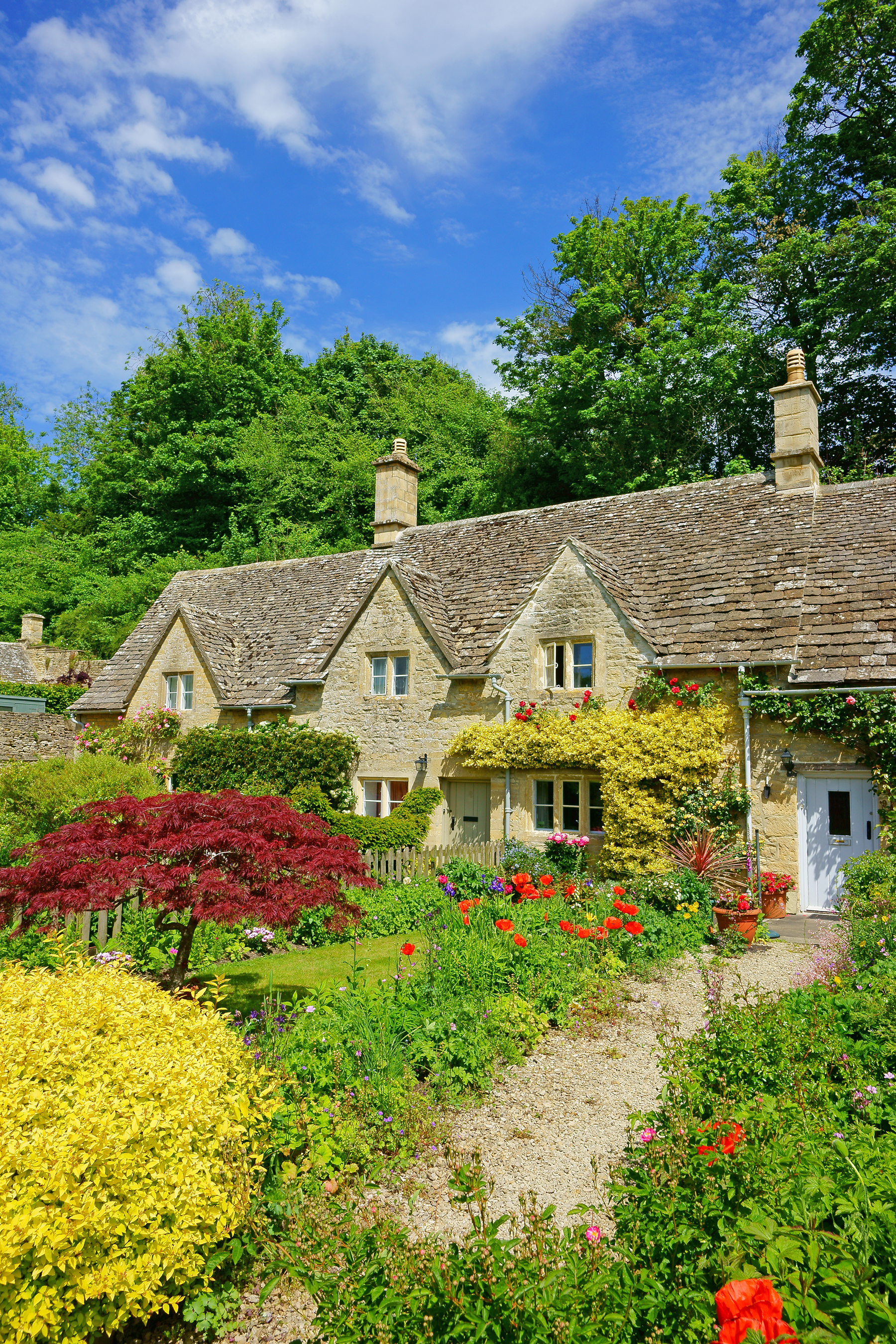 Traditionelt engelsk stenhus i Cotswolds med farverig blomsterhave og stentag