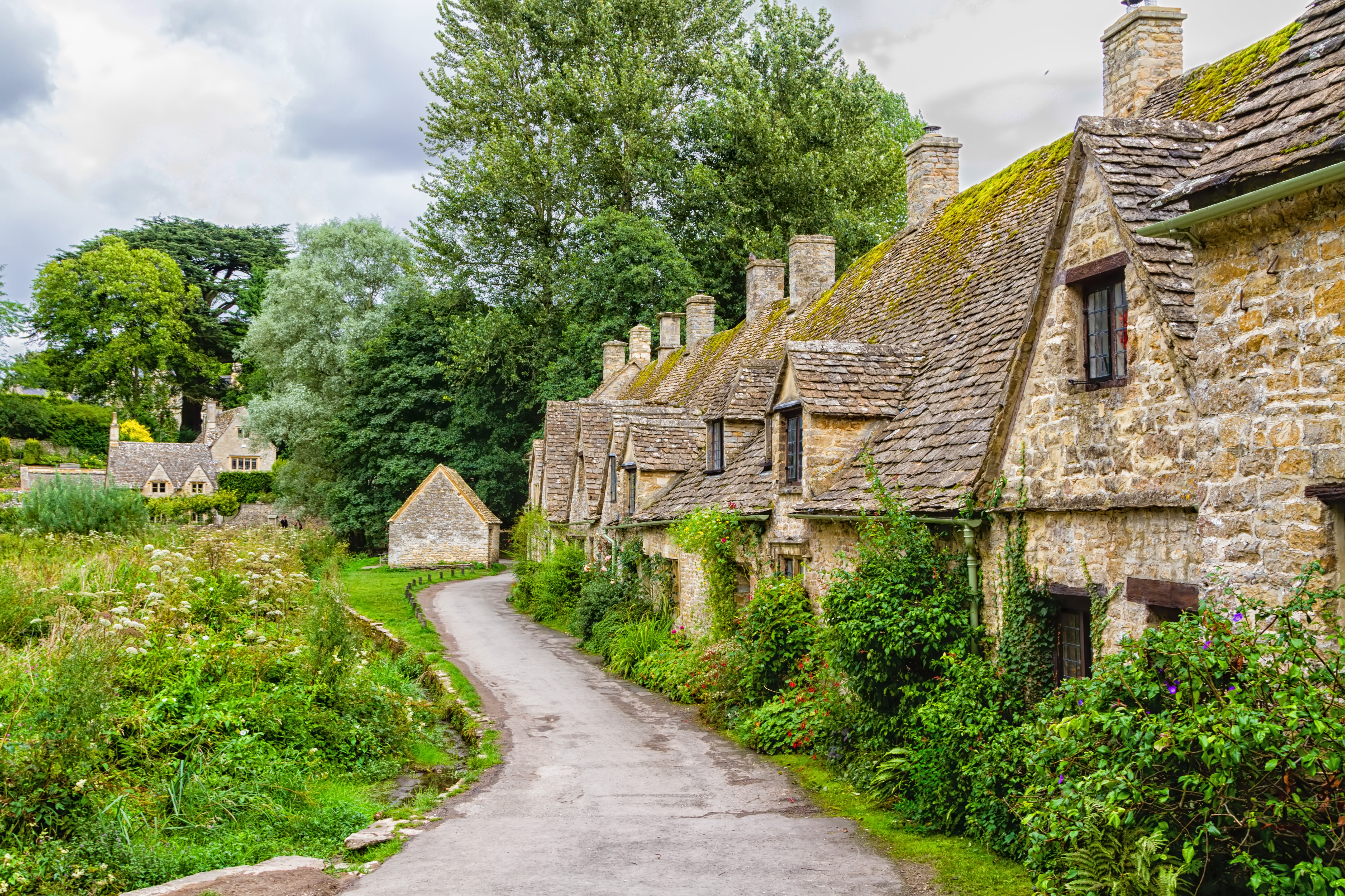 Traditionelle stenhuse i pittoresk Cotswolds-landsby med mosgroede tage og landvej
