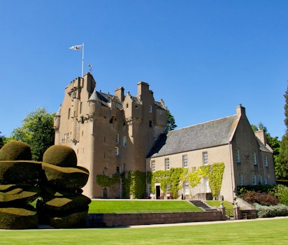 Crathes Castle i Aberdeenshire, Skotland, med smukke topiarhaver og flag i strålende solskin