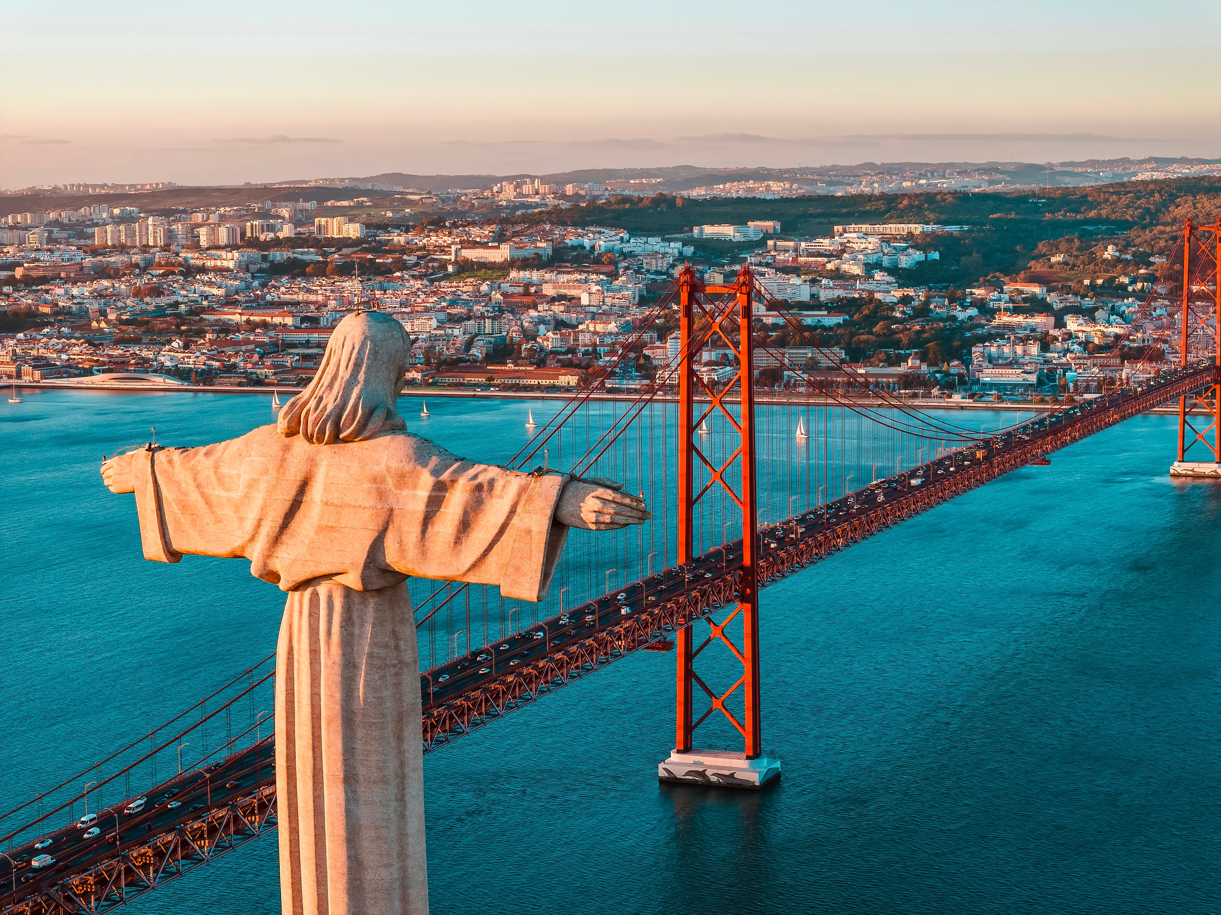 Cristo Rei statue med udsigt over Lissabons 25. april bro og Tejo floden ved solnedgang