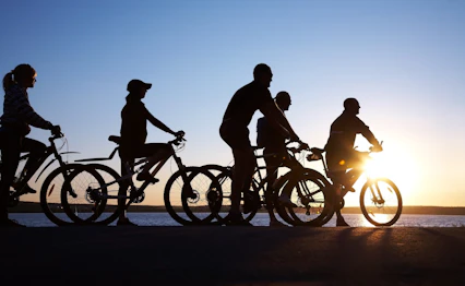 Silhuetter af venner på cykeltur langs vandet i solnedgangen - oplev glæden ved aktiv ferie og udendørs eventyr med Smil Rejser