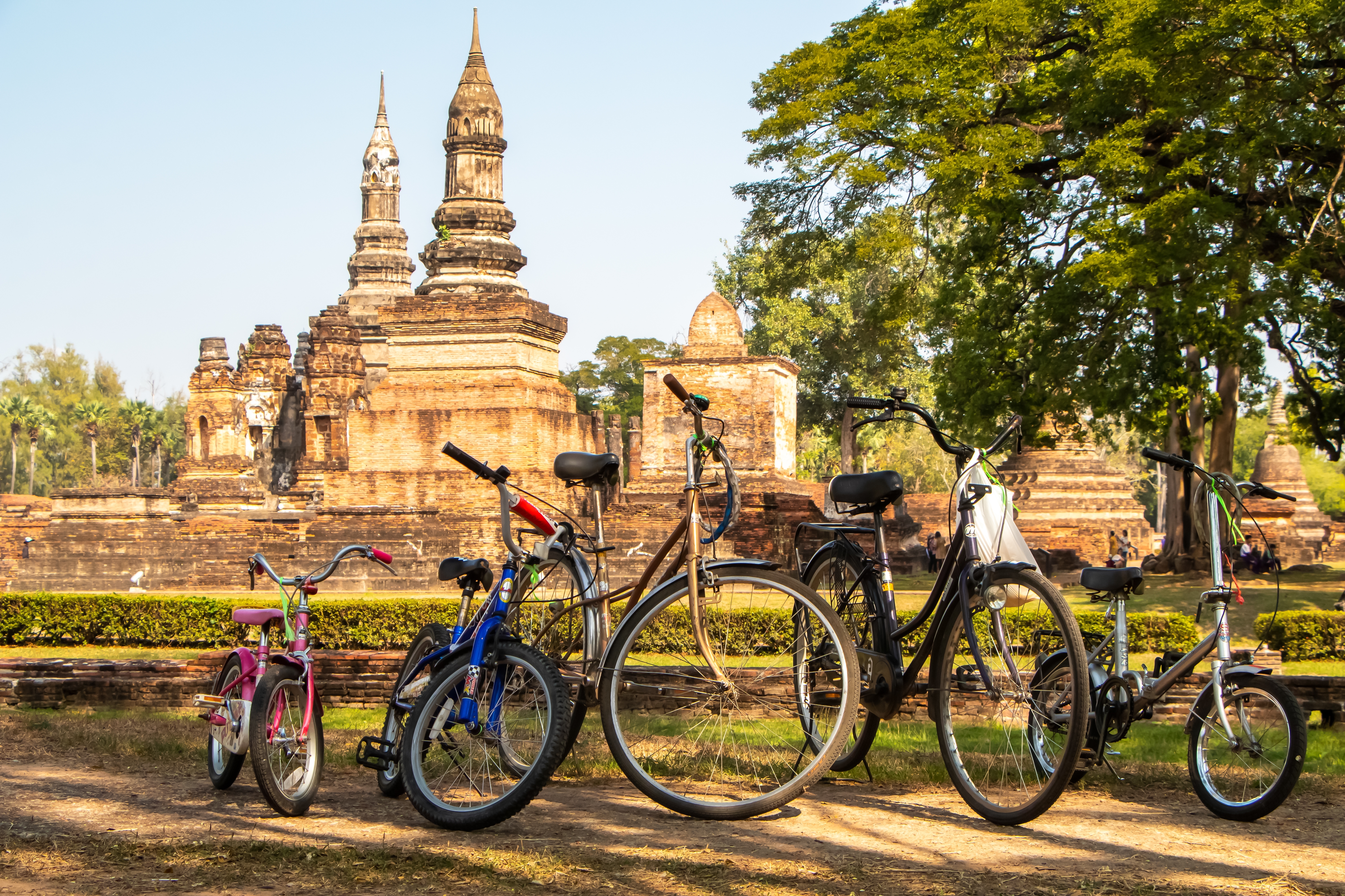 Farverige cykler parkeret foran gamle buddhistiske tempelruiner i Sukhothai Historiske Park, Thailand