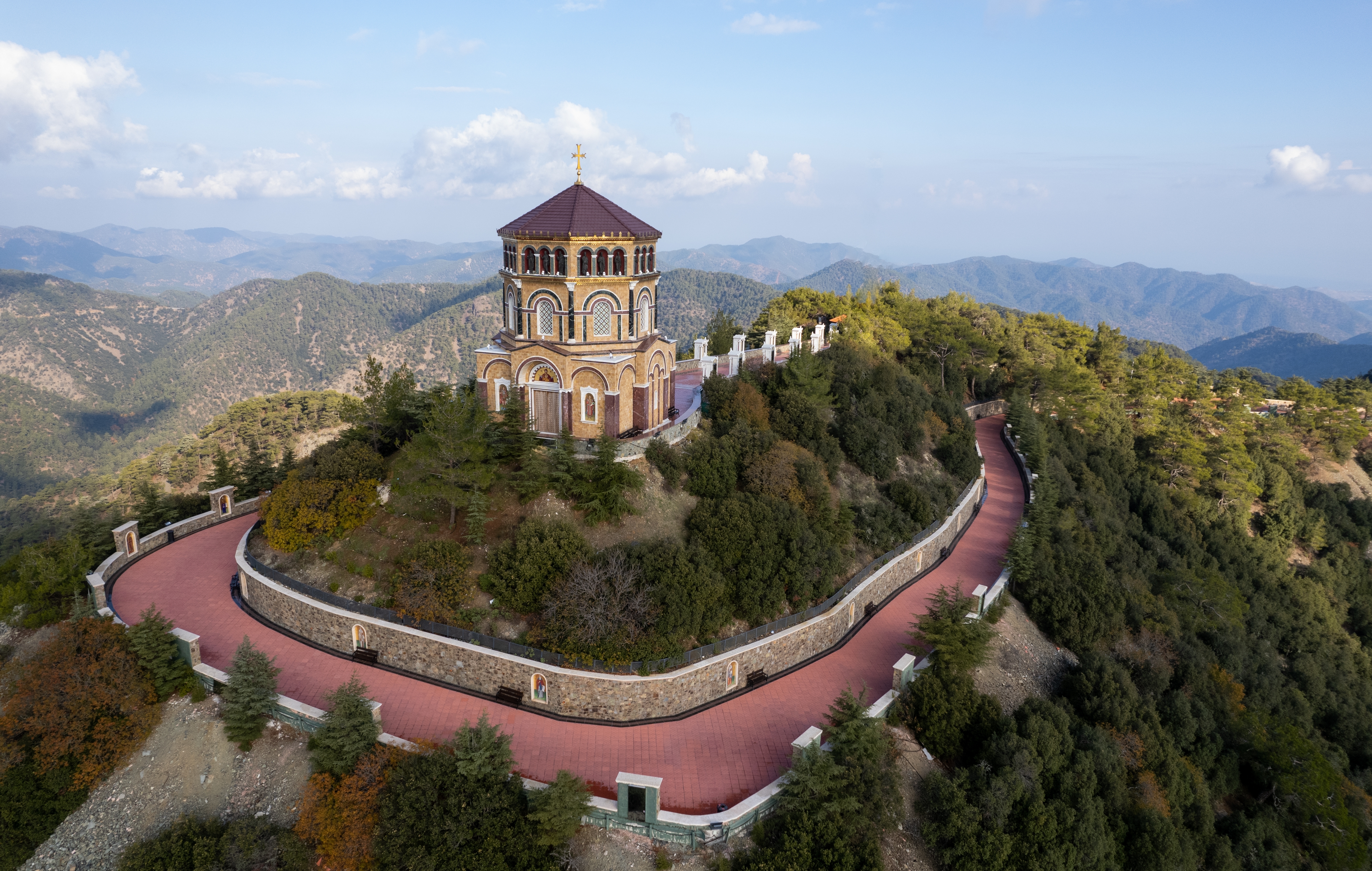 Dronefoto af Throni of Panagia Kykkos klosteret på bjergtop i Cypern med hvide bygninger omgivet af grøn skov og bjerglandskab