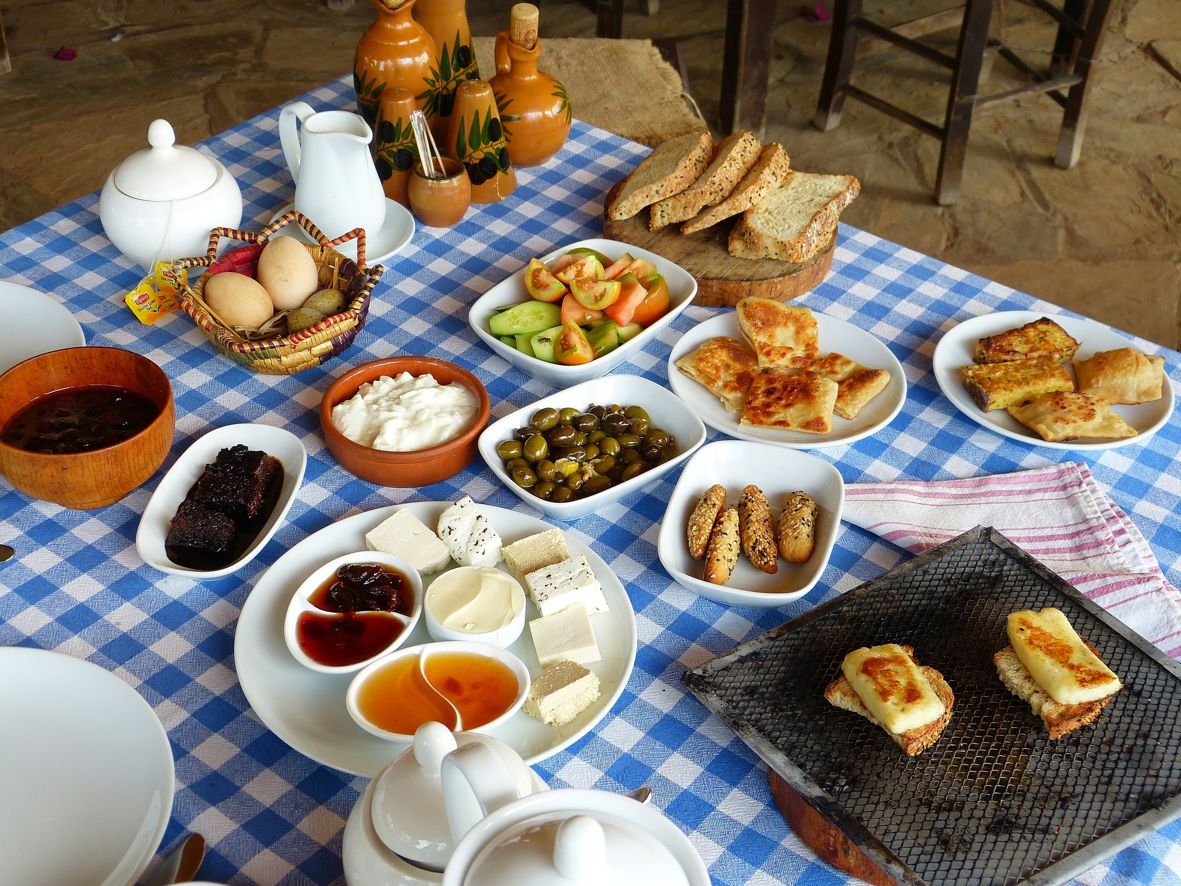Traditionel cypriotisk morgenmadsbuffet med friske oste, oliven, æg, brød og marmelade serveret på en blåternet dug
