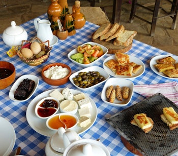 Traditionel cypriotisk morgenmadsbuffet med friske oste, oliven, æg, brød og marmelade serveret på en blåternet dug