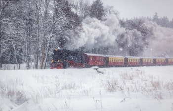 Nostalgisk dampmaskinetog kører gennem snedækket vinterlandskab med røde vogne
