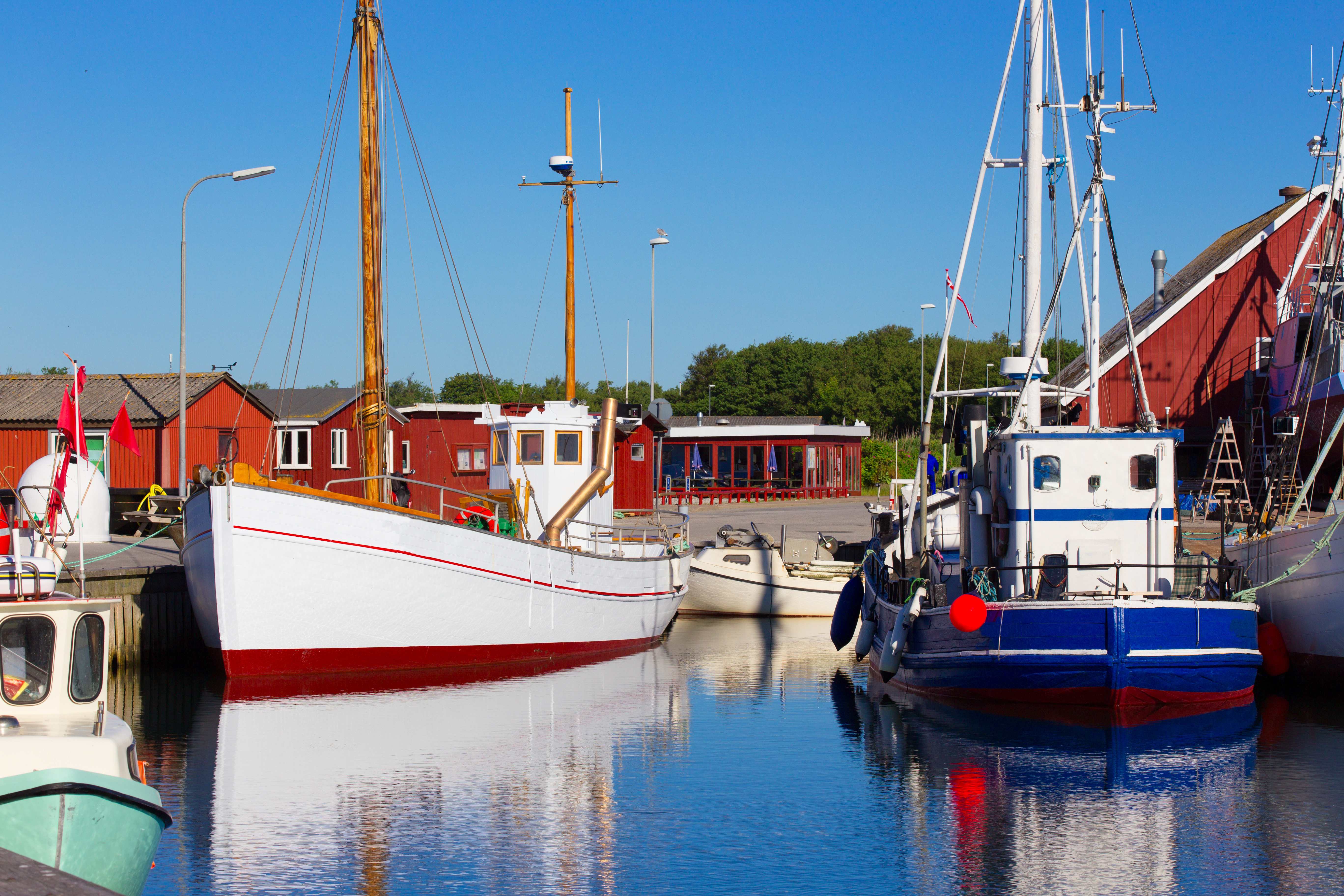 Traditionelle fiskerbåde i dansk havn med røde træhuse og blå himmel