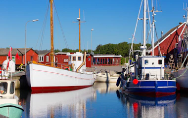 Traditionelle fiskerbåde i dansk havn med røde træhuse og blå himmel