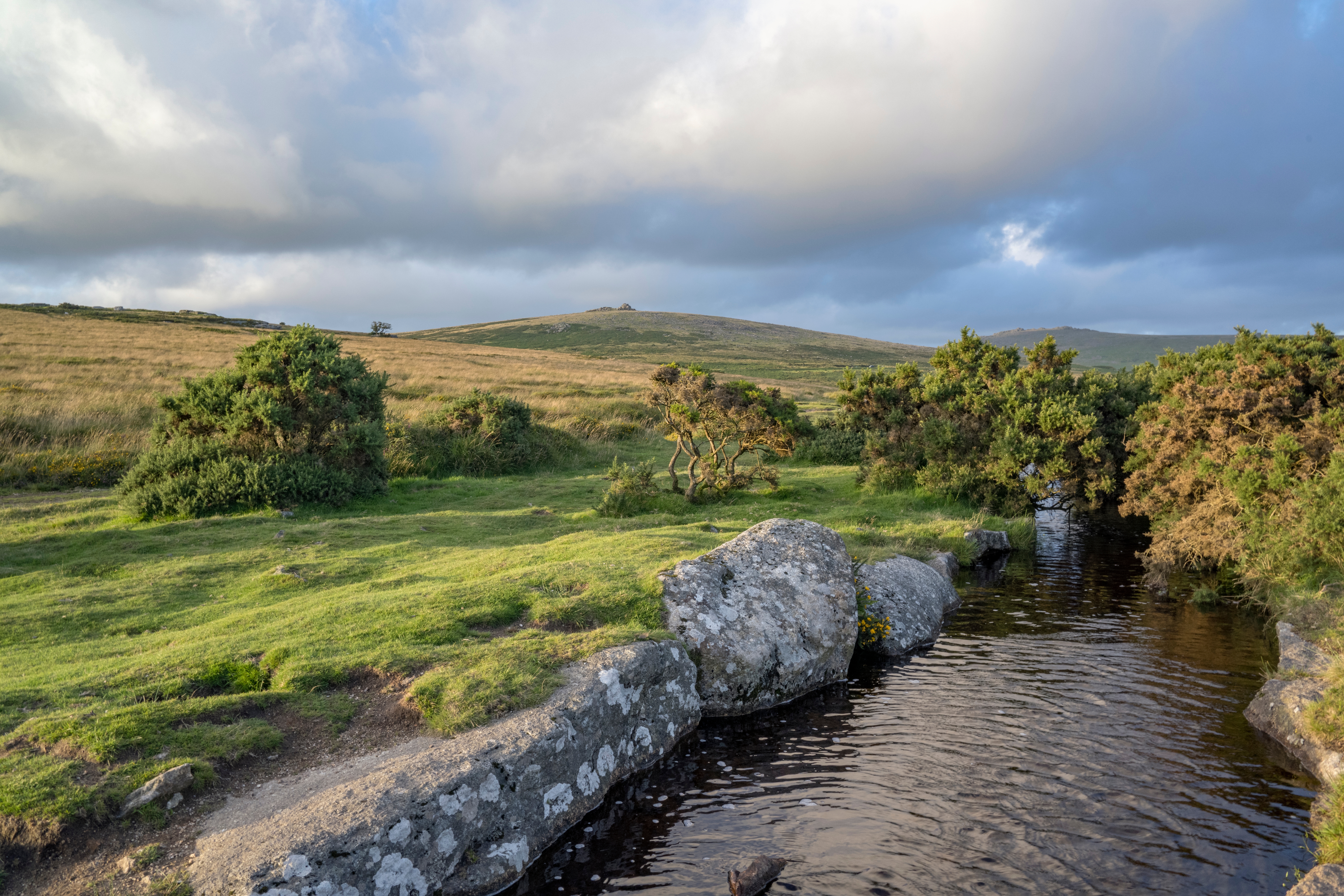Naturskønt aftenlandskab i Dartmoor Nationalpark med åbne vidder, klippeformationer og vandløb i Devon, England