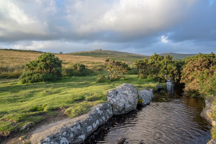 Naturskønt aftenlandskab i Dartmoor Nationalpark med åbne vidder, klippeformationer og vandløb i Devon, England
