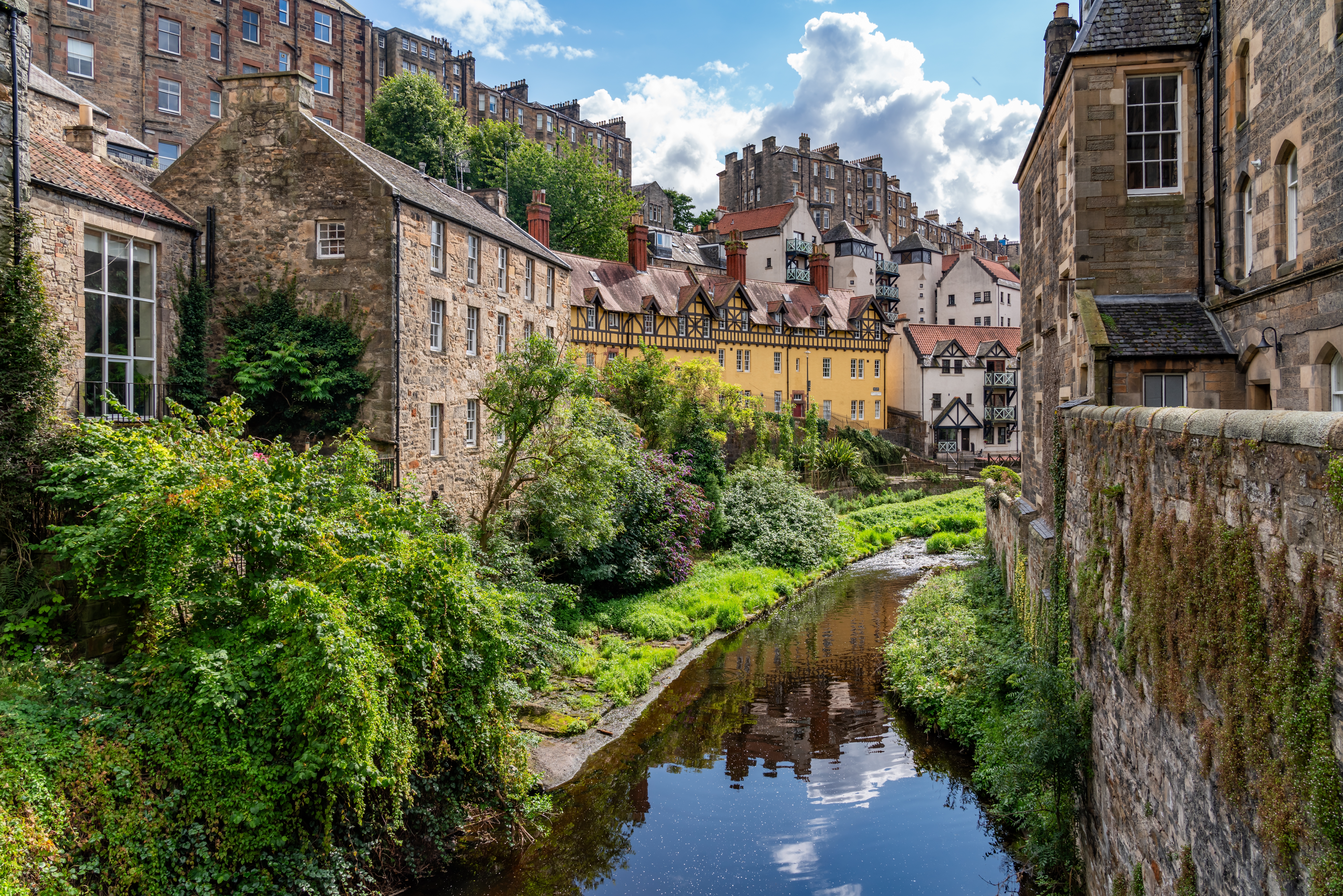 Idyllisk udsigt over Dean Village i Edinburgh, Skotland, med den fredelige flod Water of Leith omgivet af historiske stenbygninger og grønne træer