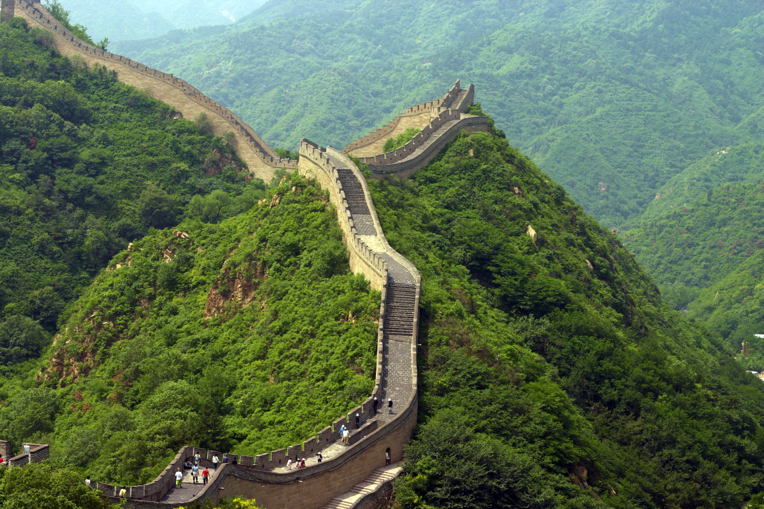 Betagende udsigt over Den Kinesiske Mur nær Beijing, der snor sig gennem grønne bjerge under klar blå himmel - et af verdens mest imponerende historiske bygningsværker