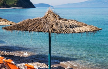 Orange solsenge med stråparasol ved den krystalklare turkisblå kyst i Dhermi, Albanien - perfekt til afslapning i solen