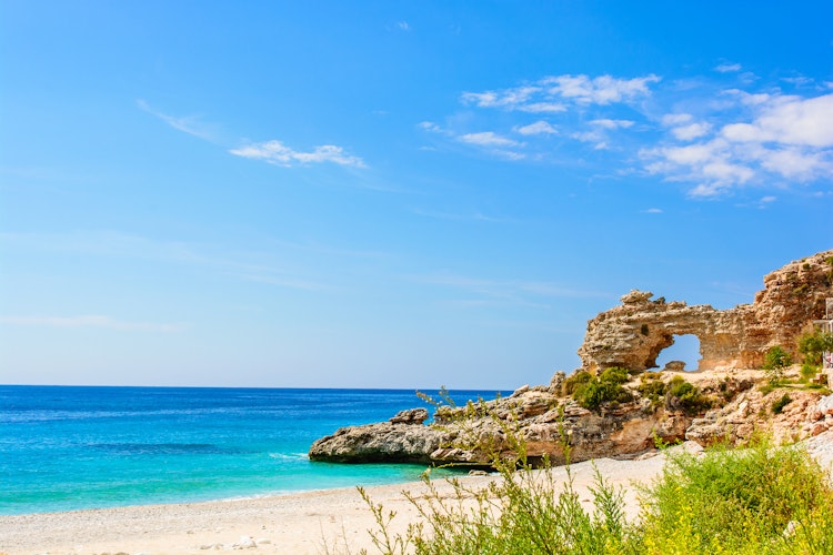 Idyllisk sandstrand med majestætiske klipper ved Det Ioniske Hav i Dhermi, Albanien - perfekt til en afslappende badeferie