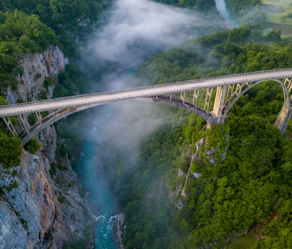 Luftfoto af den imponerende Djurdjevica bro over Tara-floden i Montenegro med morgentåge der svæver gennem den grønne canyon