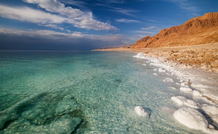 Betagende udsigt over Det Døde Havs kystlinje i Jordan med krystalklart vand, saltformationer og ørkenlandskab