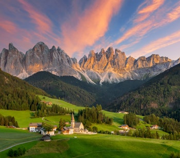 Den maleriske Santa Maddalena kirke omgivet af grønne enge i Val di Funes dalen med de majestætiske Dolomitter i baggrunden ved solnedgang
