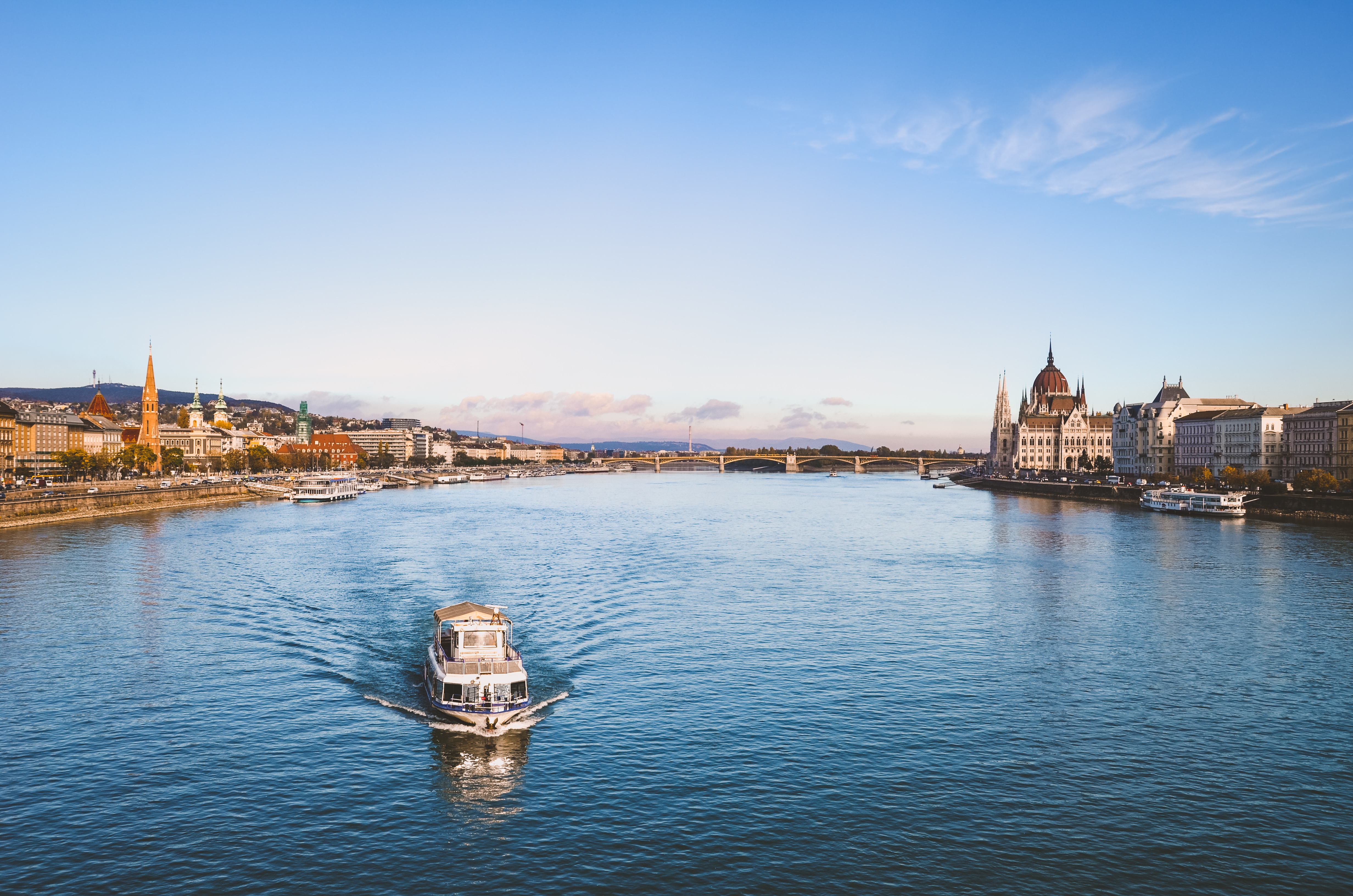Panoramaudsigt over Donaufloden i Budapest med sightseeingbåd og det historiske ungarske Parlamentsbygning under blå himmel