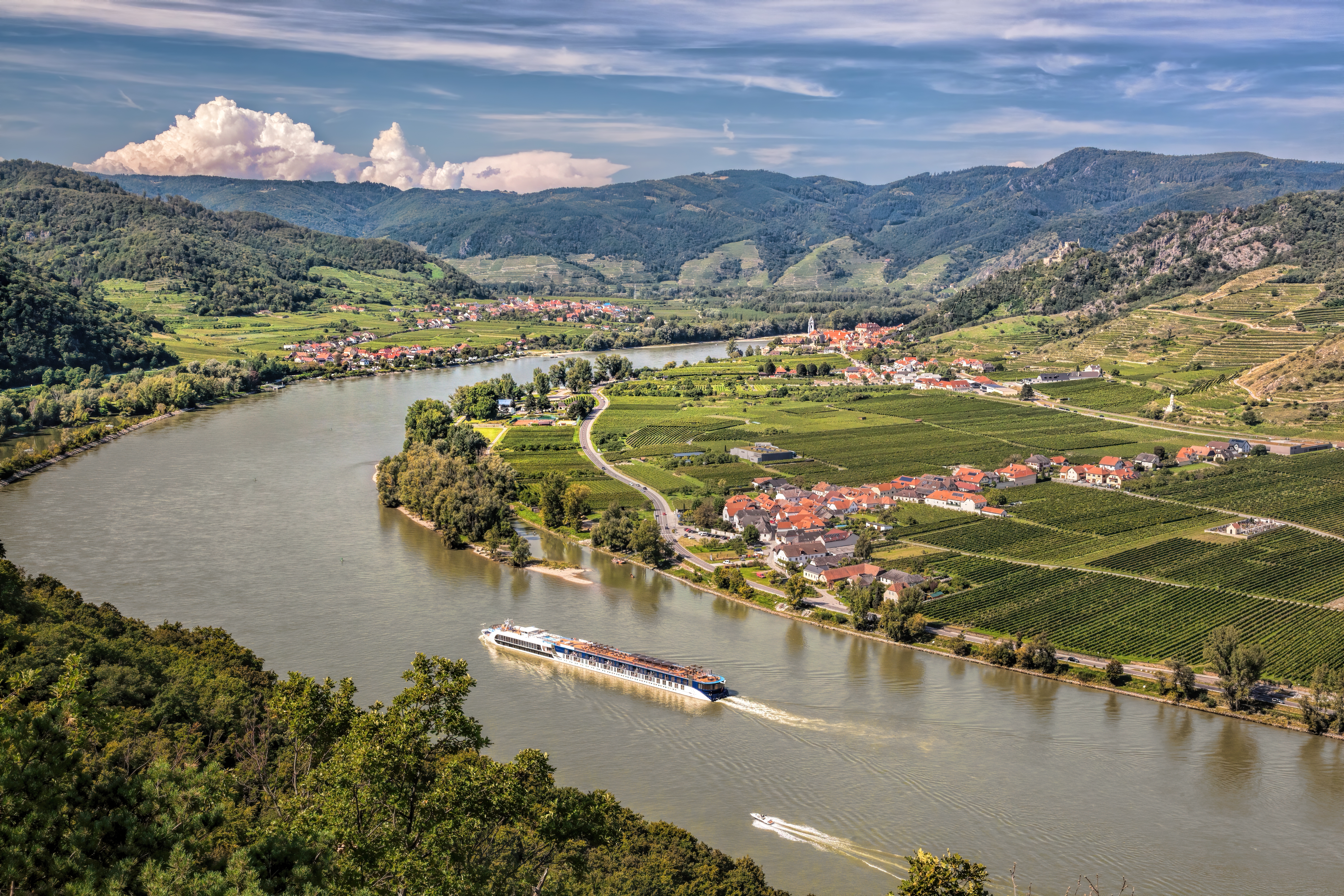 Betagende panorama over Wachau-dalen i Østrig med et flodkrydstogtskib på Donau-floden og den historiske landsby Dürnstein med sit karakteristiske blå kirketårn