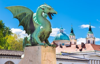 Den ikoniske grønne drageskulptur på den berømte Dragebro i Ljubljana, Sloveniens charmerende hovedstad med historisk arkitektur i baggrunden.