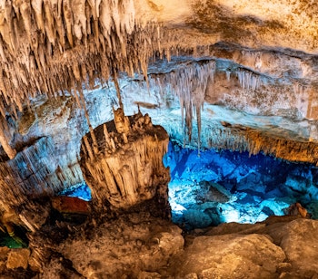 Imponerende blåt oplyst underjordisk søområde i Drach-grotterne på Mallorca med spektakulære drypsten og kalkstensformationer