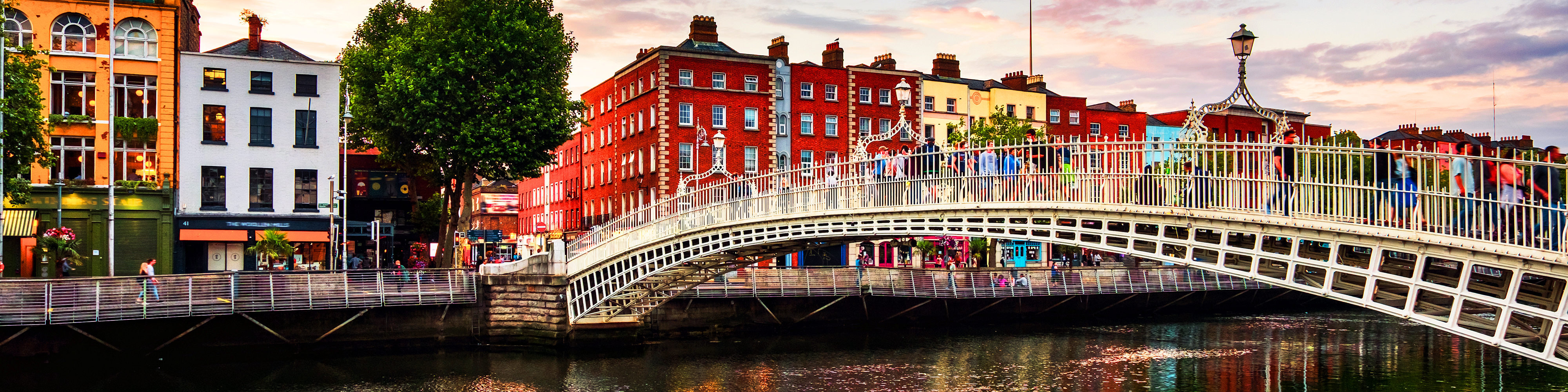 Den ikoniske Ha'penny Bridge i Dublin oplyst i aftentimerne med smuk refleksion i floden Liffey ved solnedgang