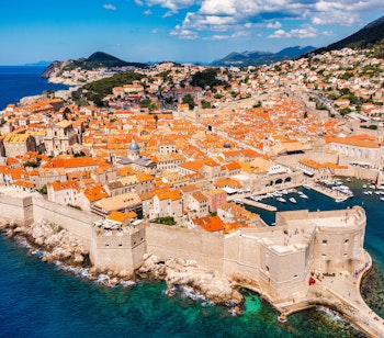 Panoramaudsigt over Dubrovniks historiske gamle bydel med karakteristiske orange tegltage, middelalderlige fæstningsmure og det azurblå Adriaterhav langs Kroatiens dalmatiske kyst.