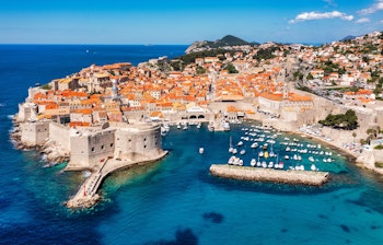 Luftfoto af Dubrovniks historiske bymidte med orange tegltage, bymure og den azurblå Adriaterhavskyst i Kroatien