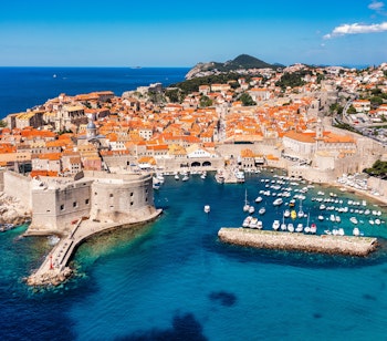 Luftfoto af Dubrovniks historiske bymidte med orange tegltage, bymure og den azurblå Adriaterhavskyst i Kroatien