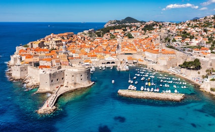 Luftfoto af Dubrovniks historiske bymidte med orange tegltage, bymure og den azurblå Adriaterhavskyst i Kroatien