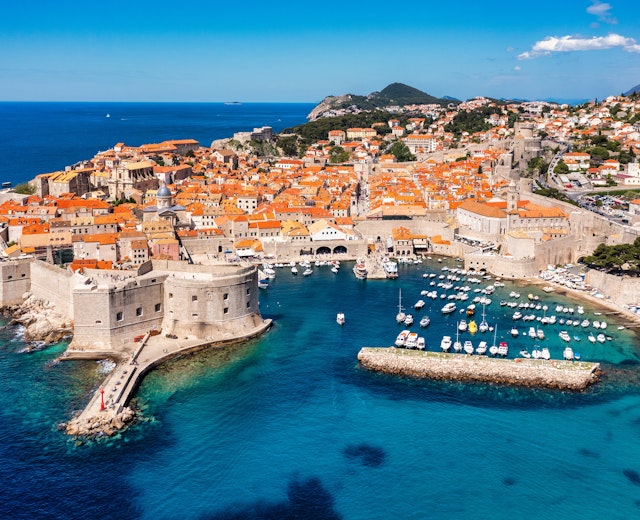 Luftfoto af Dubrovniks historiske bymidte med orange tegltage, bymure og den azurblå Adriaterhavskyst i Kroatien