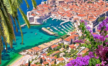 Betagende luftfoto af Dubrovniks historiske havn og gamle bydel med karakteristiske orange tegltage omgivet af middelalderlige bymure ved Adriaterhavets azurblå vand