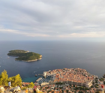 Betagende luftfoto af Dubrovniks historiske bymidte med de ikoniske røde tegltage og Lokrum øen omgivet af det azurblå Adriaterhav, set fra Srđ-bjerget i Kroatien