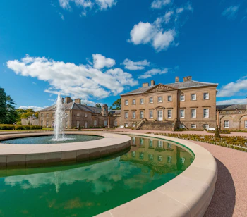 Smuk georgisk herregård ved Dumfries House i Ayrshire, Skotland, med en elegant springvandsfontæne og spejlbassin på en solrig dag