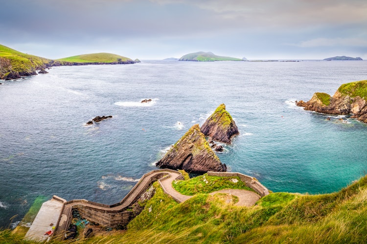 Betagende udsigt over Dunquin Havn med snoet sti, turkisblåt vand og klippeøer på Dingle-halvøen, en del af vandreruten Slea Head i Irland