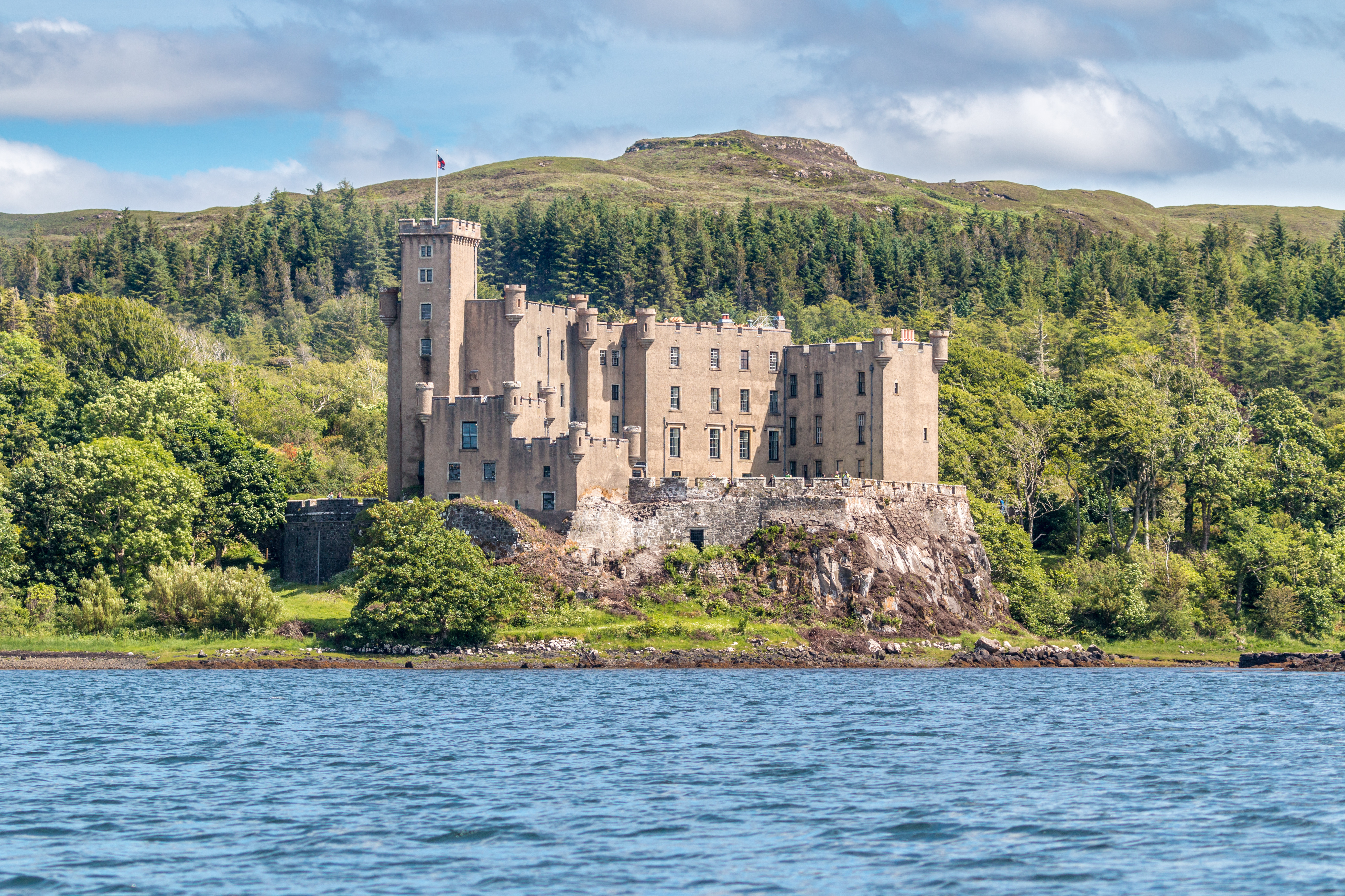 Dunvegan Castle på Isle of Skye i Skotland, majestætisk beliggende på en klippefyldt kyst omgivet af grønne skove og skotske højlandskulle