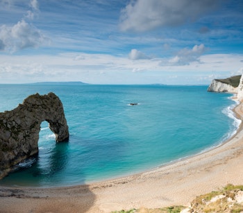 Durdle Door - den berømte naturlige stenbue ved Jurassic Coast i Dorset, England, med turkisblåt vand og gylden sandstrand