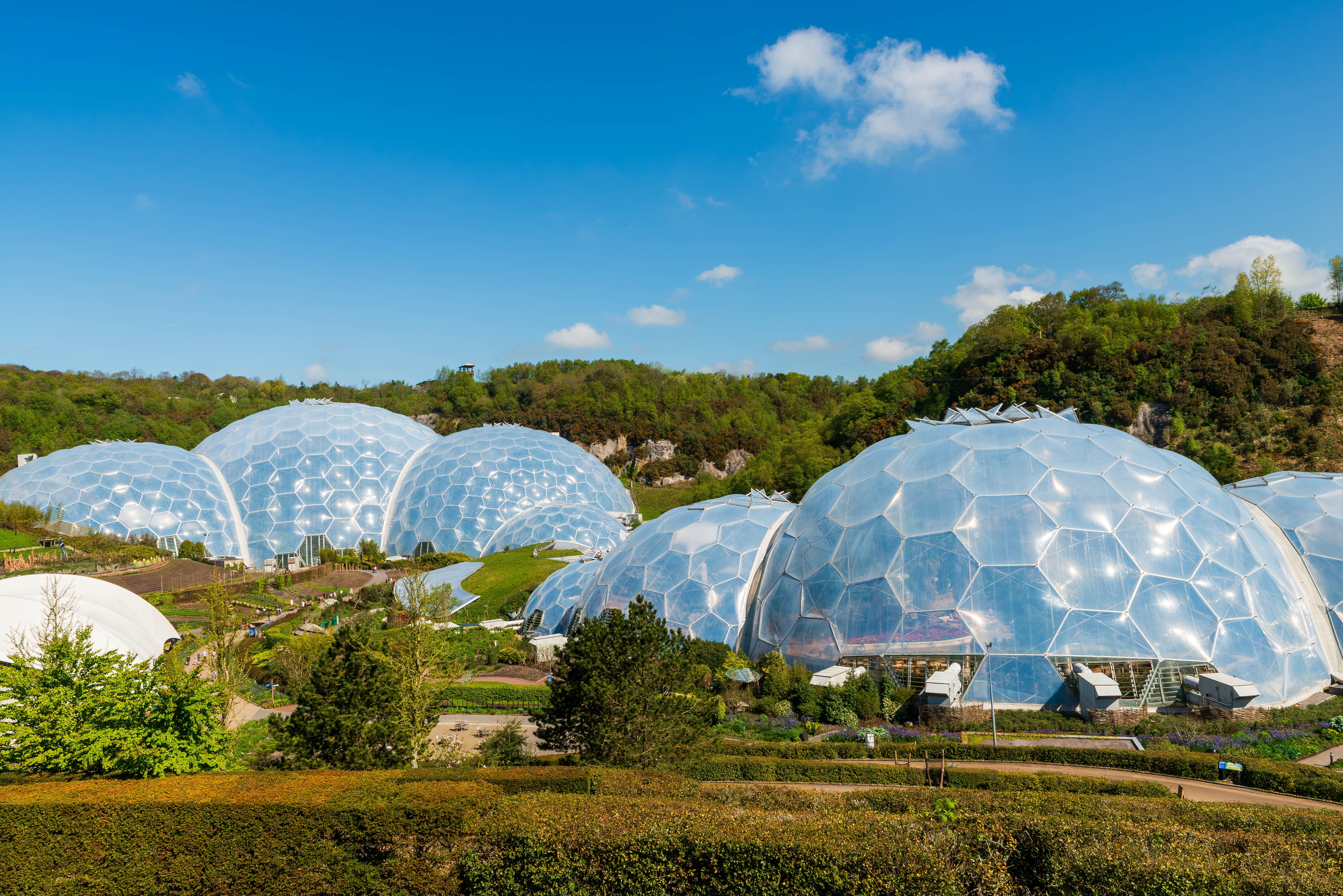 Luftfoto af Eden Project i Cornwall, England, med de karakteristiske geodætiske kupler omgivet af grønne områder i et tidligere lergravningsområde, kendt for sin bæredygtige tilgang til miljø og uddannelse.
