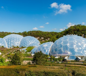 Luftfoto af Eden Project i Cornwall, England, med de karakteristiske geodætiske kupler omgivet af grønne områder i et tidligere lergravningsområde, kendt for sin bæredygtige tilgang til miljø og uddannelse.