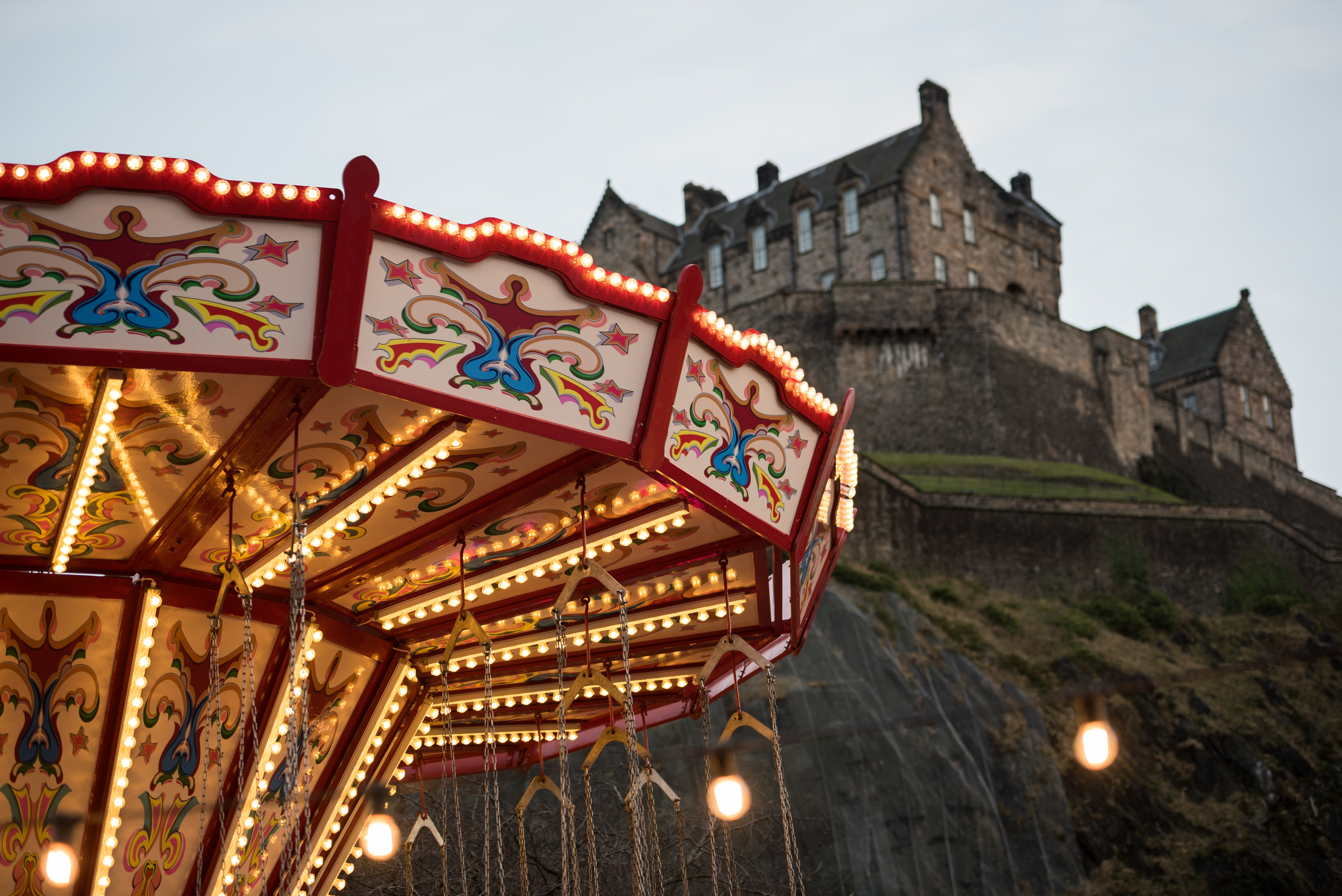 Oplyst karrusel med gynger ved Edinburgh Christmas market med Edinburgh Castle dramatisk placeret på klippen i baggrunden