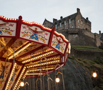 Oplyst karrusel med gynger ved Edinburgh Christmas market med Edinburgh Castle dramatisk placeret på klippen i baggrunden